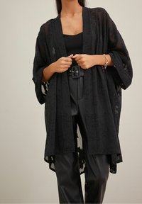 Czarny przezroczysty kimono z kwiatowym wzorem, z szerokimi rękawami, otwarte z przodu, nałożone na czarny dopasowany top i skórzane spodnie z wysokim stanem.