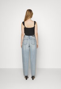 Top preto cropped com alças franzidas, combinado com calças de ganga de perna larga e de cintura alta em azul claro. O modelo usa sapatos de salto pretos; fundo branco liso.