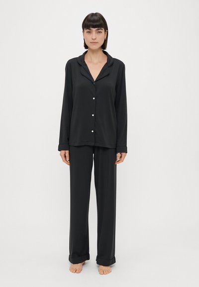 Black pajamas made of smooth fabric, featuring a collared, button-up shirt and loose-fitting, cuffed pants. No patterns or accents present.