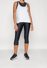 Vitt idrottstanktopp med svart designdetalj, parat med svarta knälånga leggings och svarta sportskor. Släta, åtsittande material.