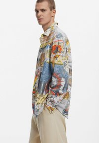 Colorful button-up shirt featuring various graphic prints, primarily in yellow, red, blue, and green, with a relaxed fit and long sleeves.