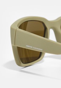 Brune tonede solbriller med en mat lys beige stel. Har en firkantet form og "Armani Exchange" indgraveret på stangen.