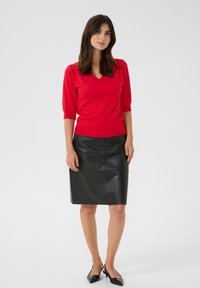 Punainen v-pääntie neulepusero, jossa on lyhyet puffihihat, yhdistetty mustaan nahkainen kynähameeseen, joka on sileä ja polvipituinen.