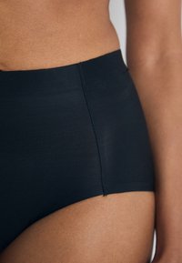 Chiloți negri, cu talie înaltă, cu o textură netedă și un brâu elastic, având cusături plate pentru a fi cât mai puțin vizibili sub îmbrăcăminte.