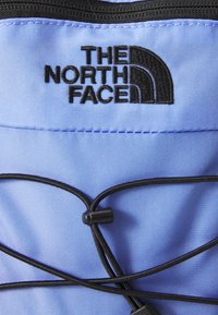 Kék szövet, sima tapintással, fekete "The North Face" logóval. Rugalmas zsinórok és húzókák a beállításhoz.