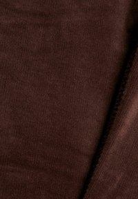 Gros plan sur un tissu en velours côtelé marron foncé montrant de fines nervures verticales et un bord plié avec des coutures visibles.