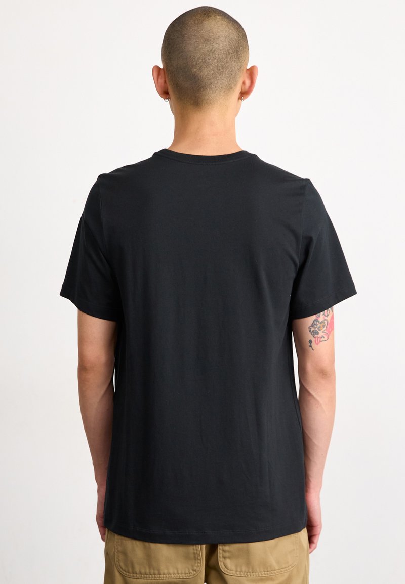 Czarny bawełniany t-shirt z klasycznym okrągłym dekoltem, krótkimi rękawami i gładką fakturą; eksponuje widoczny tatuaż na przedramieniu.