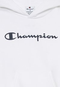Hvit hettegenser med frontlomme, med en fremtredende sort "Champion" logo i kursiv. Myk stoff med snor i hetten.