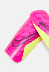 Rosa Fußballschienbeinschoner mit einem Wabendesign, gelben Akzenten, schwarzem Branding und abgerundeten Kanten für Schutz und Komfort.