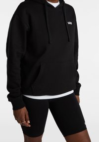 Sudadera negra de mezcla de algodón con un bolsillo frontal, cordones y un logo blanco. Combinada con pantalones cortos de bicicleta negros.