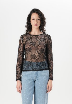 Black lace long-sleeve top with floral pattern, sheer fabric, round neckline, and relaxed fit, paired with light blue jeans featuring studded accents.