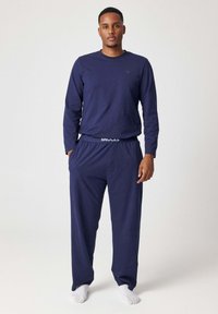 Top a maniche lunghe color blu navy e pantaloni abbinati realizzati in tessuto morbido. I pantaloni hanno una cintura elasticizzata con il logo “SNOCKS”. Vestibilità standard, stile casual.