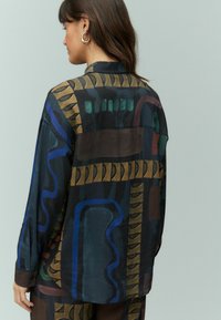 Camicia a maniche lunghe in tessuto leggero, caratterizzata da motivi astratti in colori scuri, con accenti verdi, blu e dorati. Vestibilità comoda e colletto.