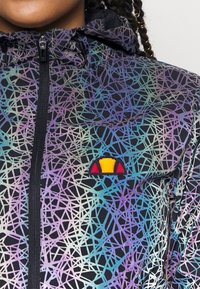 Huvtröja i svart med ett färgglatt geometriskt mönster. Har en dragkedjestängning och en liten broderad logotyp i gult, rött och blått.