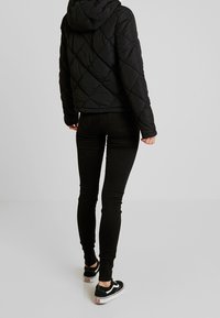 Black quilted puffer jacket with a hood, fitted to the waist, paired with black skinny jeans and black sneakers with white accents.