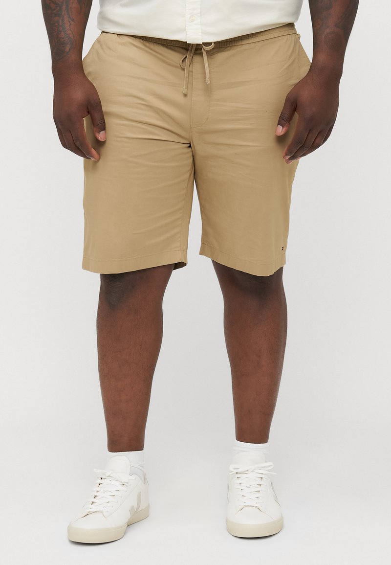 Khaki shorts in a lightweight fabric with an elastic waist and drawstring. Features a straight-cut hem. Worn with white sneakers and socks.