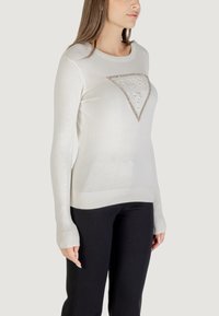 Suéter blanco de manga larga con dobladillo acanalado, que presenta un logo triangular texturizado adornado con pedrería en la parte delantera.