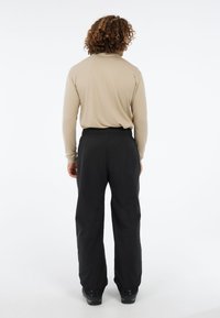 Lange beige shirt met aansluitende mouwen, gecombineerd met losse zwarte broek. De outfit heeft een soepele textuur en een elastische tailleband. Zwarte schoenen zichtbaar.