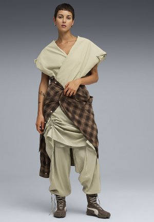 Hellgrünes Wickeltop mit kurzen Ärmeln, beige geraffter Rock, kariertes braunes Hemd um die Taille gebunden und braune Schnürstiefeletten.