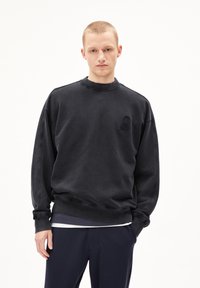 Black sweatshirt made of cotton blend, featuring a crew neck, ribbed cuffs, and an embossed logo on the left chest. Smooth texture.