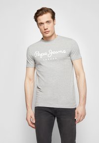 Pelēka kokvilnas T-krekls ar baltu "Pepe Jeans London" tekstu. Īsām piedurknēm, apaļa kakla izgriezuma un gluda tekstūra. Nēsā ar tumšiem džinsiem.