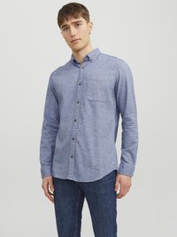 Camisa azul de botones con un bolsillo en el pecho, hecha de una tela texturizada. Manga larga, dobladillo redondeado, con botones marrones y un cuello.