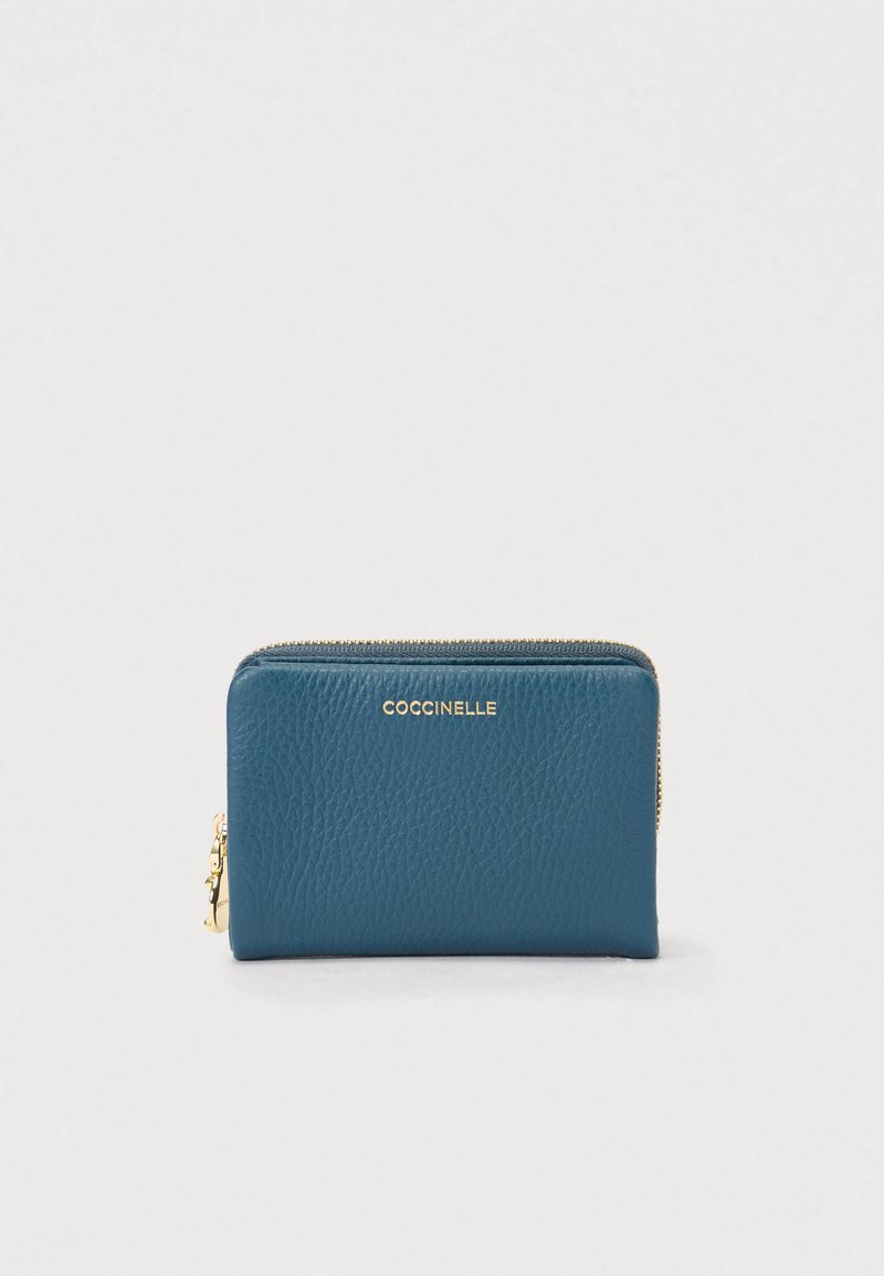 Γαλάζιο δερμάτινο πορτοφόλι με υφή και χρυσό φερμουάρ, με το όνομα μάρκας "Coccinelle" σε χρυσά γράμματα στο μπροστινό μέρος.
