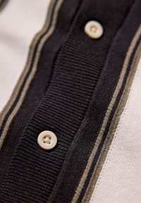 Skjorta med knapp-up som har en svart och vit randig design med ribbad yta, krämfärgade knappar och subtila accentstygningar.