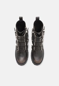 Bottes noires à la cheville en cuir texturé, avec plusieurs boucles métalliques et une semelle en caoutchouc robuste. Elles possèdent un design fonctionnel dans l'ensemble.