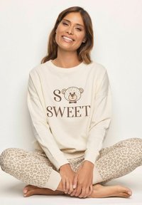 Felpa crema con la scritta "SO SWEET" e una grafica di un orso, abbinata a pantaloni da pigiama beige con stampa leopardata, entrambi caratterizzati da un tessuto morbido e una vestibilità comoda.