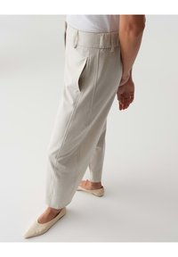 Helle beigefarbene, verkürzte Hosen mit glatter Textur, die vorne Falten und eine lockere Passform aufweisen. Getragen mit beigen, spitzen Ballerinas.