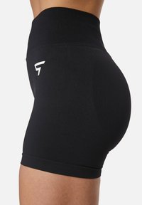 Pantaloni corti sportivi neri con vita alta, realizzati in un materiale elastico. Presentano un logo bianco sul lato e una superficie liscia.