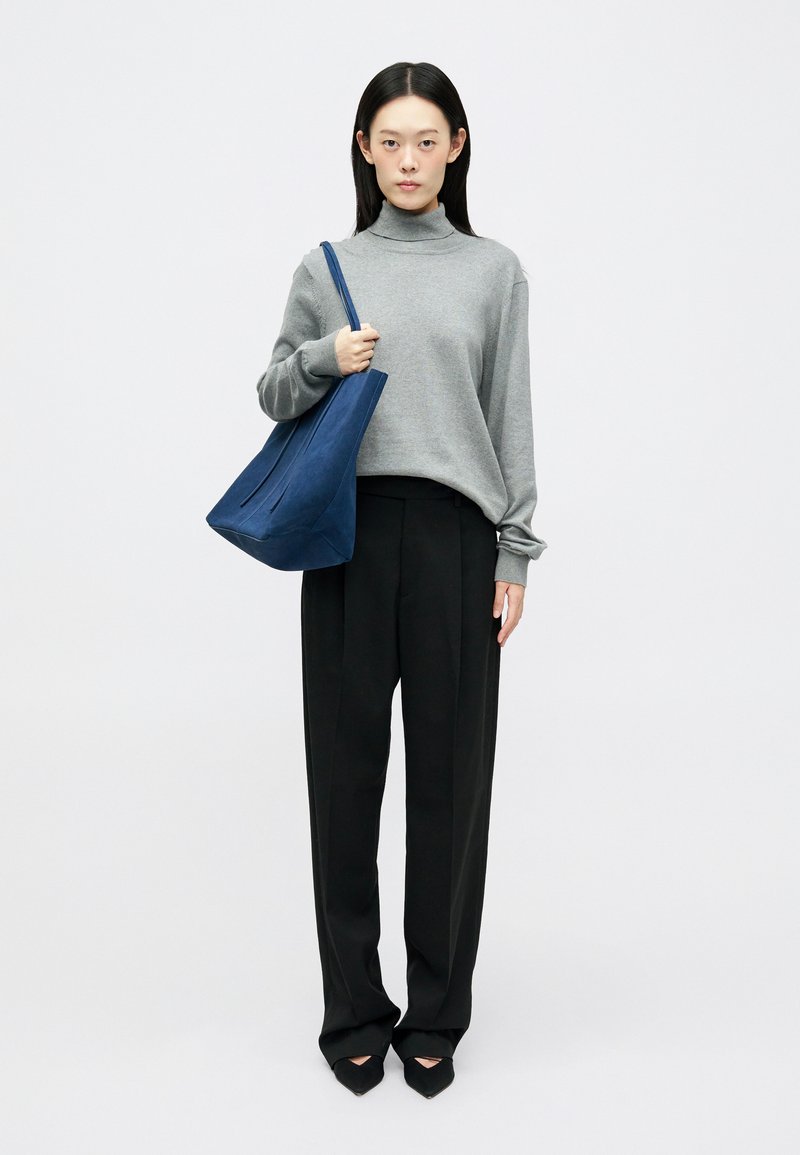 Maglione grigio a colletto alto, vestibilità morbida. Pantaloni neri a gamba larga. Borsa a tracolla blu navy con design minimalista, texture liscia. Tacchi neri a punta.