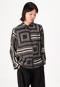 Long-sleeve black and cream button-up shirt featuring geometric line patterns, a pointed collar, and loose fit with dropped shoulders.