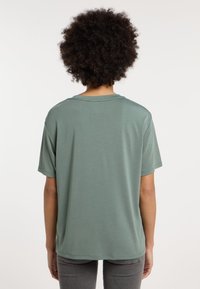 T-shirt verde a maniche corte realizzato in tessuto morbido, con una vestibilità comoda e un collo rotondo. La vista posteriore mostra una costruzione senza cuciture.
