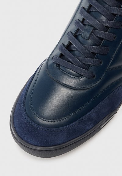 Sneaker bleu marin cu superior din piele și suede, cu șireturi asortate și talpă din cauciuc negru, prezentat dintr-un unghi frontal.