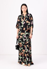 Set s cvetličnim vzorcem v črni barvi, ki vključuje oversized srajco in maxi krilo. Material se zdi lahek in teksturiran.