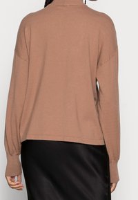 Brązowy sweter dzianinowy z wysokim kołnierzem, obniżonymi ramionami i długimi, lekko bufiastymi rękawami. Charakteryzuje się luźnym, skróconym krojem oraz miękką teksturą.