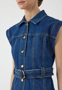 Jeanskjole med krage, korte ermer og gullfargede knapper. Har belte i midjen og vertikal søm, i en mellomblå nyanse.