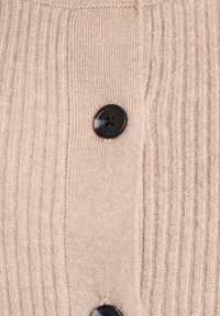 Béžový žebrovaný sveter na detailnom záberu s čiernymi plastovými gombíkmi a mäkkou textúrou, zvýrazňujúci vertikálny pletený vzor.