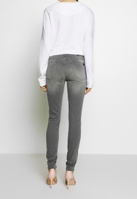 Šedé skinny džíny s vybledlým efektem a dvěma zadními kapsami, doplněné bílým topem s dlouhým rukávem. Vzhled dotváří béžové sandály na vysokém podpatku.