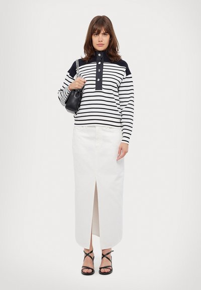 Rutet svart og hvitt langermet topp med knappet krage, kombinert med et hvitt skjørt med en frontal splitt, og svarte sandaler med remmer.