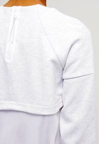 Ljusgrå sweatshirt med texturerat tyg, med hög krage, dragkedja baktill och ett nätparti nedtill.