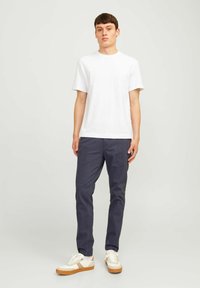 Biała bawełniana koszulka, ciemnoniebieskie spodnie i białe trampki z jasnobrązowymi akcentami. Slim fit, krótkie rękawy i minimalne elementy wzornicze.