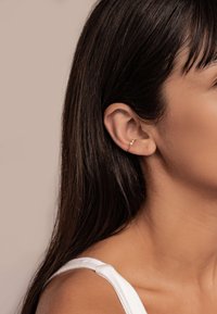 Goldener Creolenohrring mit drei kleinen sphärischen Akzenten, der eine glatte Oberfläche und ein minimalistisches Design aufweist. Am oberen Ohr getragen.