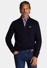 Marineblauwe pullover trui met een ritskraag, gemaakt van zachte stof. Draag het over een lichtblauw overhemd met kraag, gecombineerd met donkere spijkerbroek.