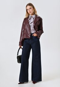 Bordeaux nepleren dubbelzijdige jas, gestreepte blouse, wijde donkerdenim jeans, zwarte handtas, en bordeauxpuntige hakken.