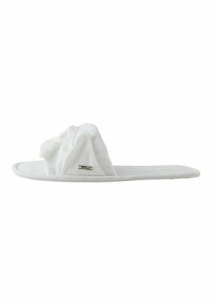 Zapatilla slide de tela blanca suave con una correa superior retorcida y una pequeña etiqueta de marca en el lateral, mostrada de lado sobre un fondo blanco.