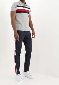 Grå pikétröja med marinblå, vit och röd horisontell rand; kombinerad med marinblå byxor med röda och vita sidoränder och vita sneakers.