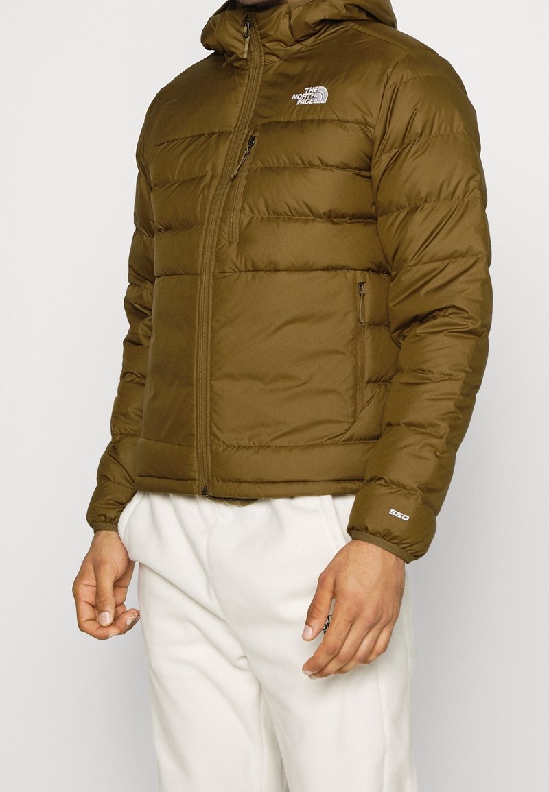 Olive green puffer jacket with a zip front, hood, and elastic cuffs. Features the North Face logo on the chest and a side pocket.